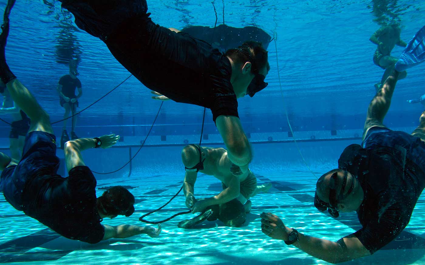 Instructors watch a tudent demonstrate knot-tying skills during water proficiency training.